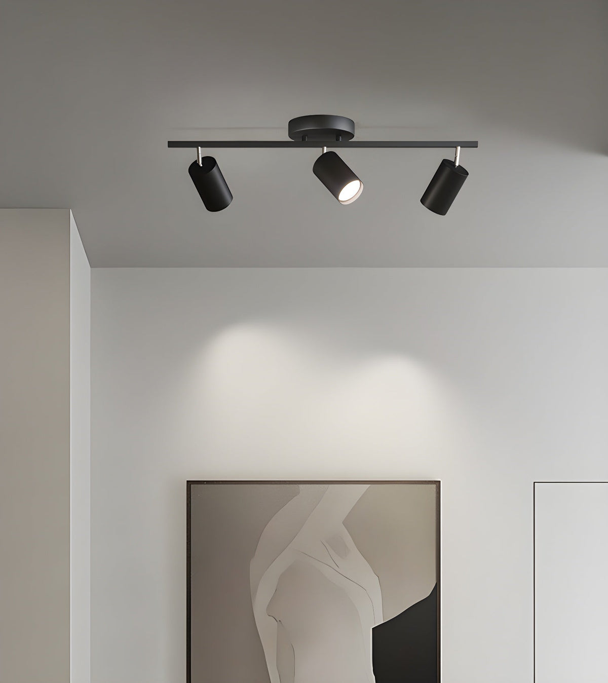 A black Clérachic three-head track light on a white ceiling washes the wall with light above a framed monochrome print.