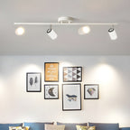 Four white Clérachic spotlight heads on a slim bar light a wall of framed prints above a sofa with blue cushions.