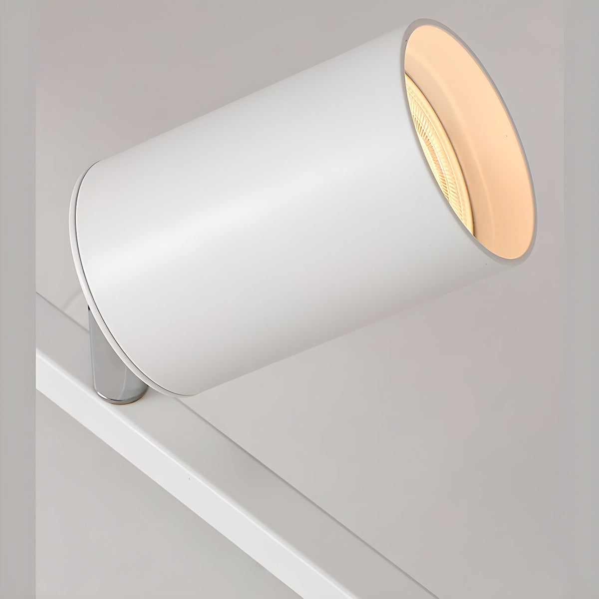 Close view of a white Clérachic spotlight head tilted on its chrome pivot, mounted on the white bar.