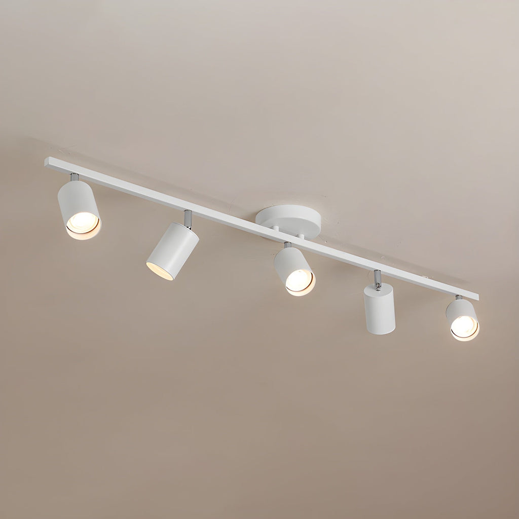 A white Clérachic five-head track light on a warm beige ceiling, with the heads pointing in different directions.