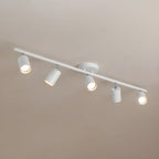 A white Clérachic five-head track light on a warm beige ceiling, with the heads pointing in different directions.