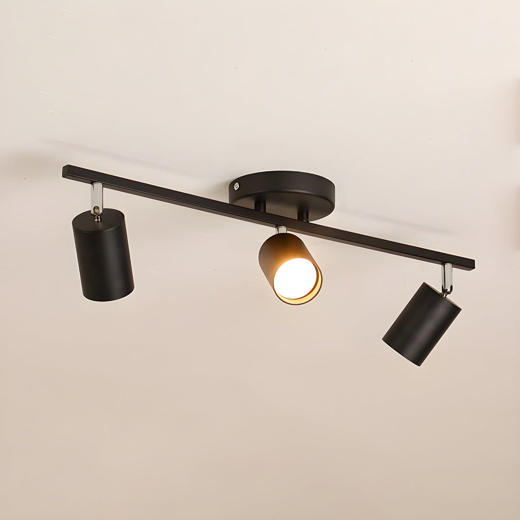A black Clérachic three-head track light with a round canopy, one head lit, against a soft beige ceiling.