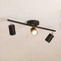 A black Clérachic three-head track light with a round canopy, one head lit, against a soft beige ceiling.