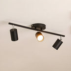 A black Clérachic three-head track light with a round canopy, one head lit, against a soft beige ceiling.