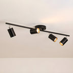 A black Clérachic four-head track light on a beige ceiling, with a round canopy and gold-lined heads.