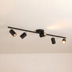 A black Clérachic five-head track light along a beige ceiling, its gold-lined heads angled in different directions.