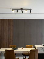Black Clérachic five-head track light on a white ceiling above a marble table and tan chairs, in a room panelled in grey.