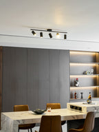 Five adjustable heads on a black Clérachic track light above a marble dining table with leather chairs and a lit shelf of bottles.