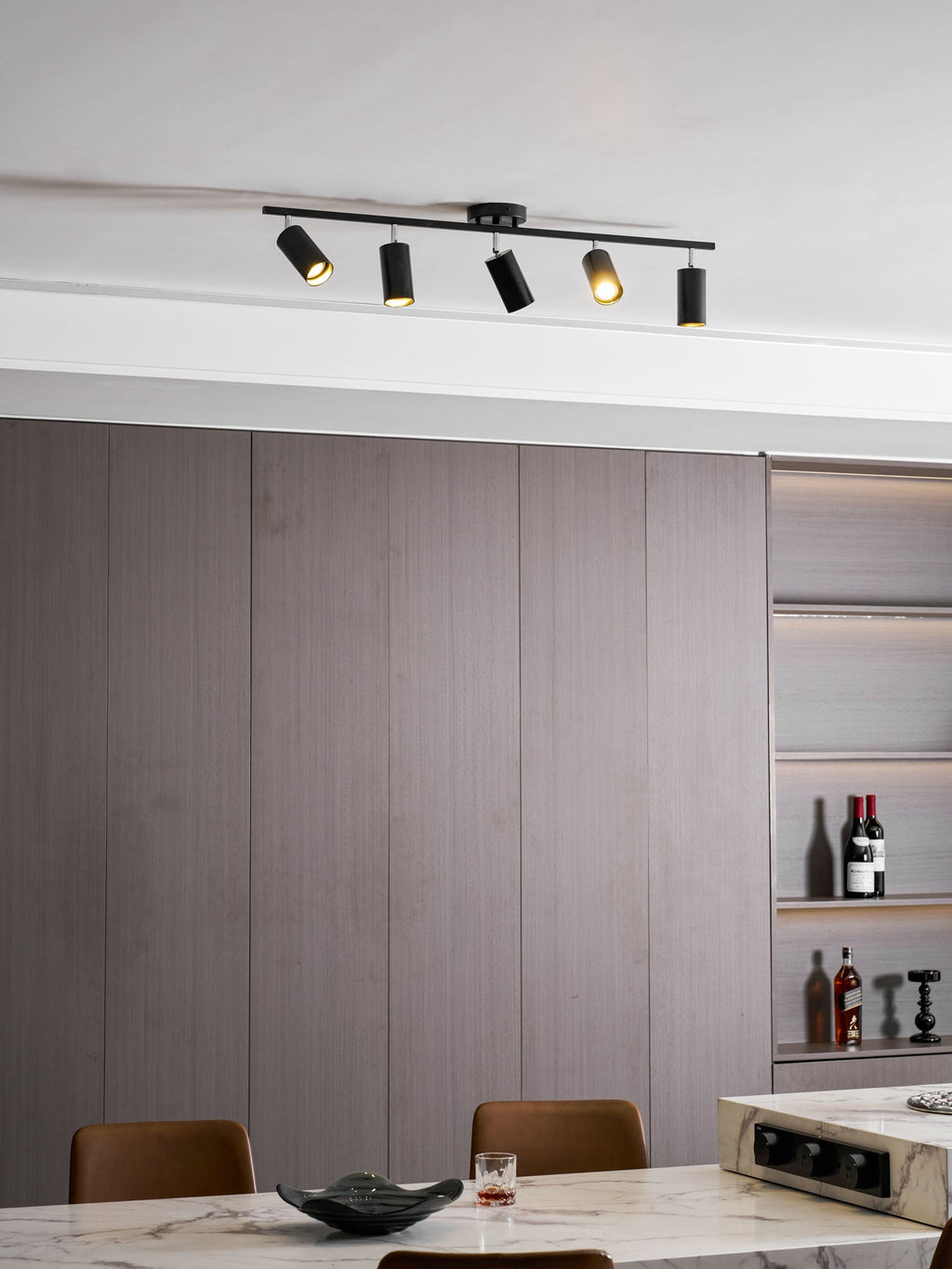 Clérachic five-head track light in black on a ceiling above grey wall panels and a marble table with a dark bowl.