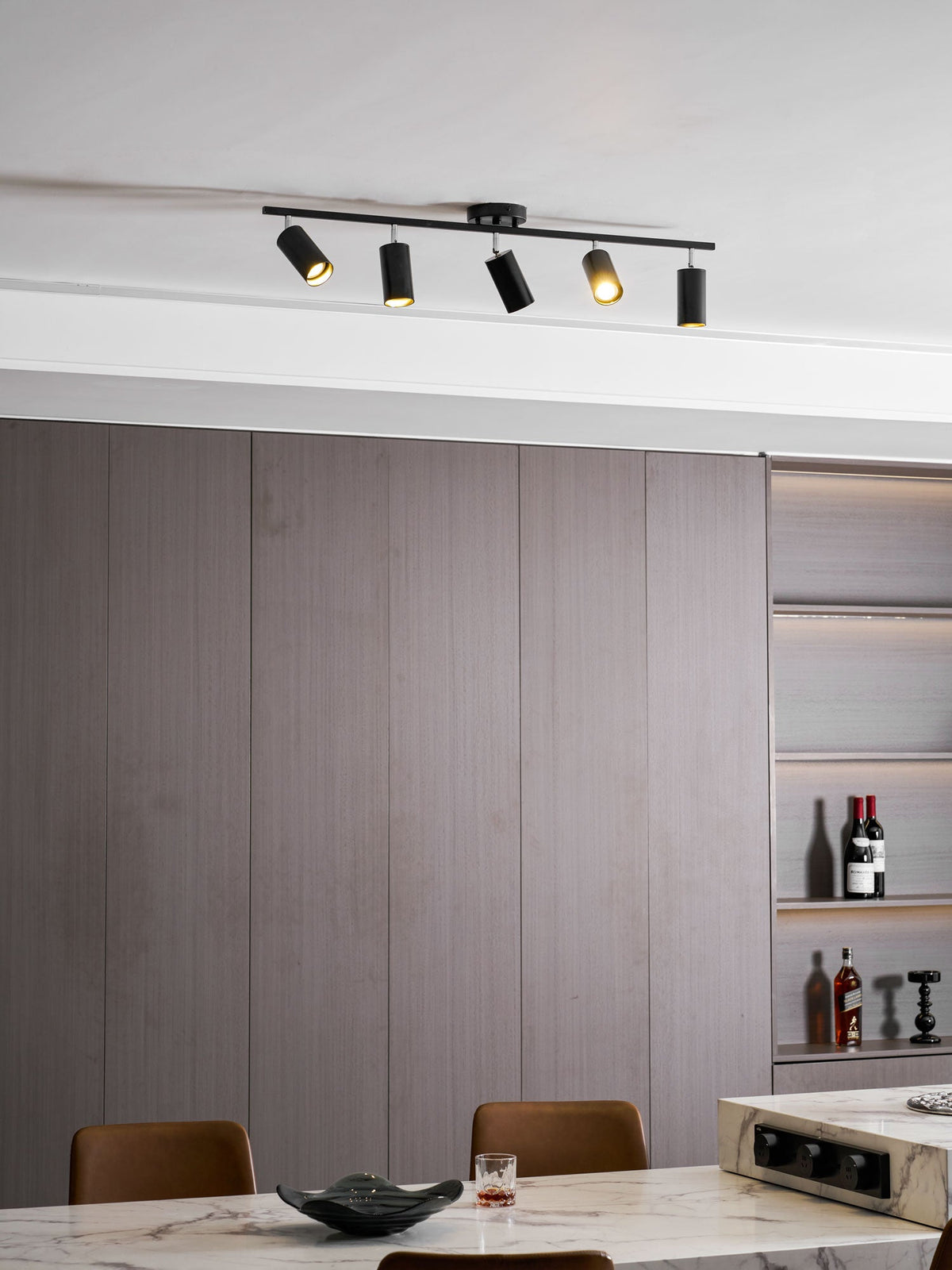 Clérachic five-head track light in black on a ceiling above grey wall panels and a marble table with a dark bowl.