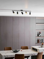 Black five-head track light by Clérachic over a dining room with a marble table, tan chairs and a lit wine shelf.