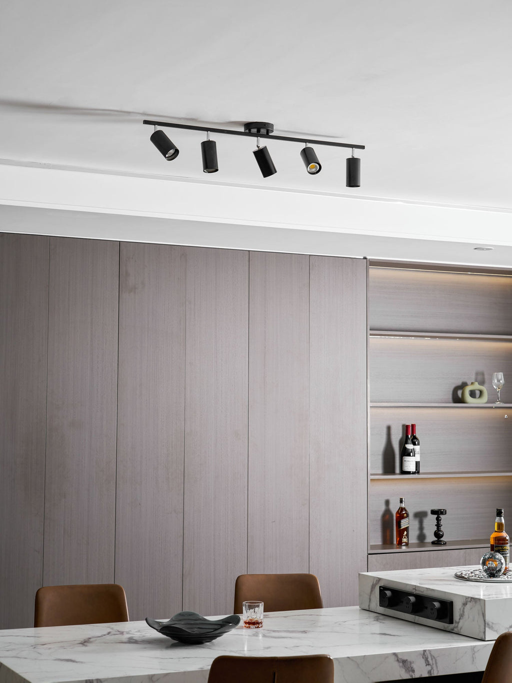 A black Clérachic track light with five heads, seen from a lower angle against grey panelling and a bottle shelf.
