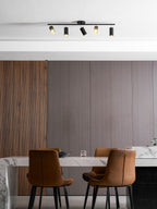 Close view of a black Clérachic five-head track light above a dining table, with ribbed walnut panelling and two tan chairs.