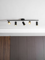 Lit black Clérachic five-head track light with a round canopy above a ribbed walnut wall panel.