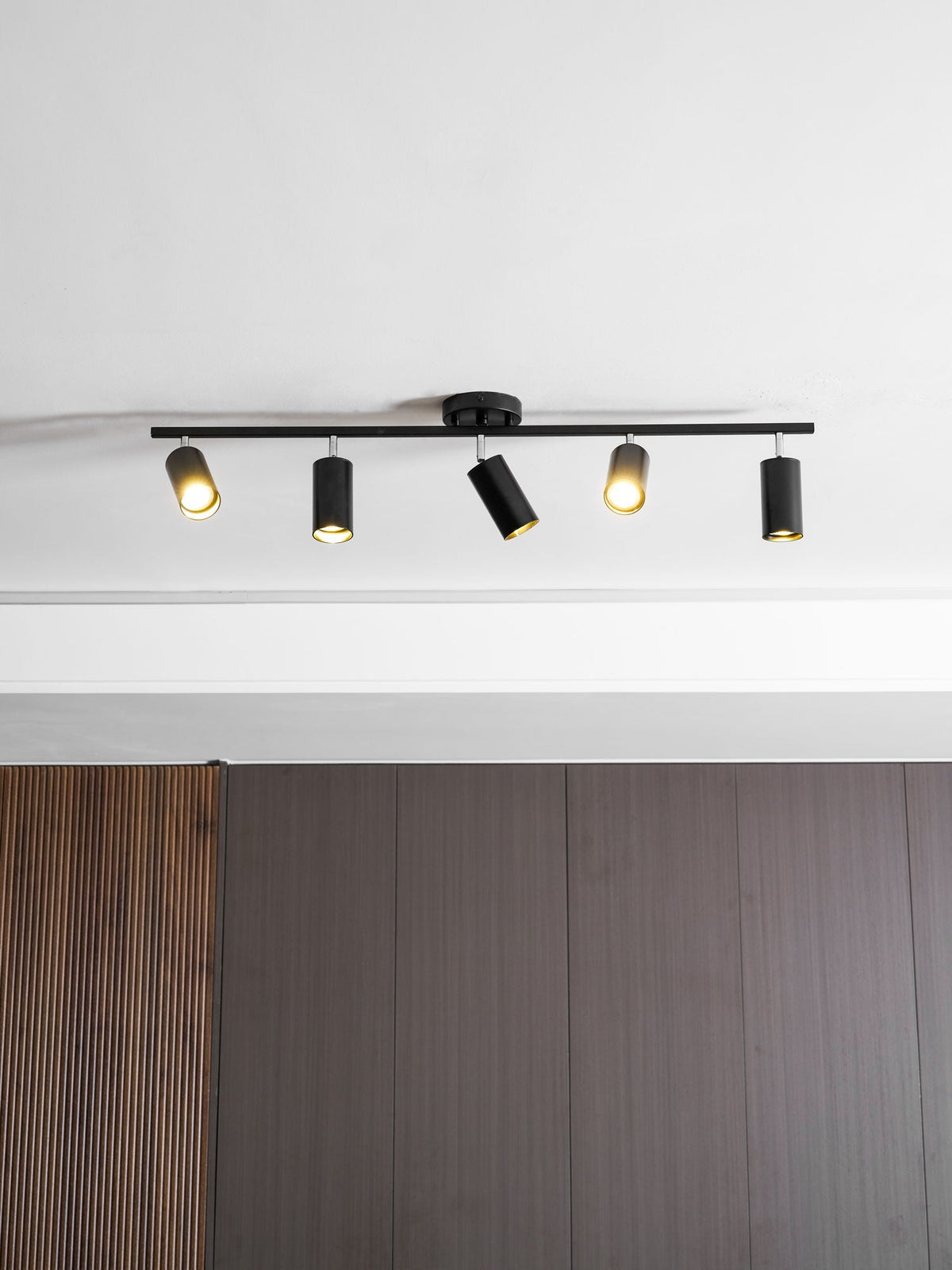 Lit black Clérachic five-head track light with a round canopy above a ribbed walnut wall panel.