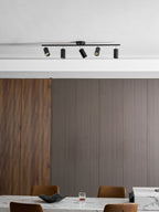 Black Clérachic track light with five heads on a ceiling above ribbed wood panelling and a marble table with tan chairs.