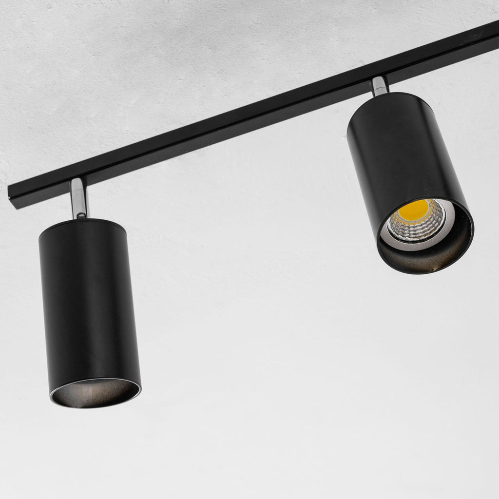Close view of two black Clérachic spotlight heads on a slim black bar, one with its warm bulb showing.