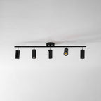 Overhead view of a black Clérachic five-head track light on a white ceiling, one head lit and the others pointing down.