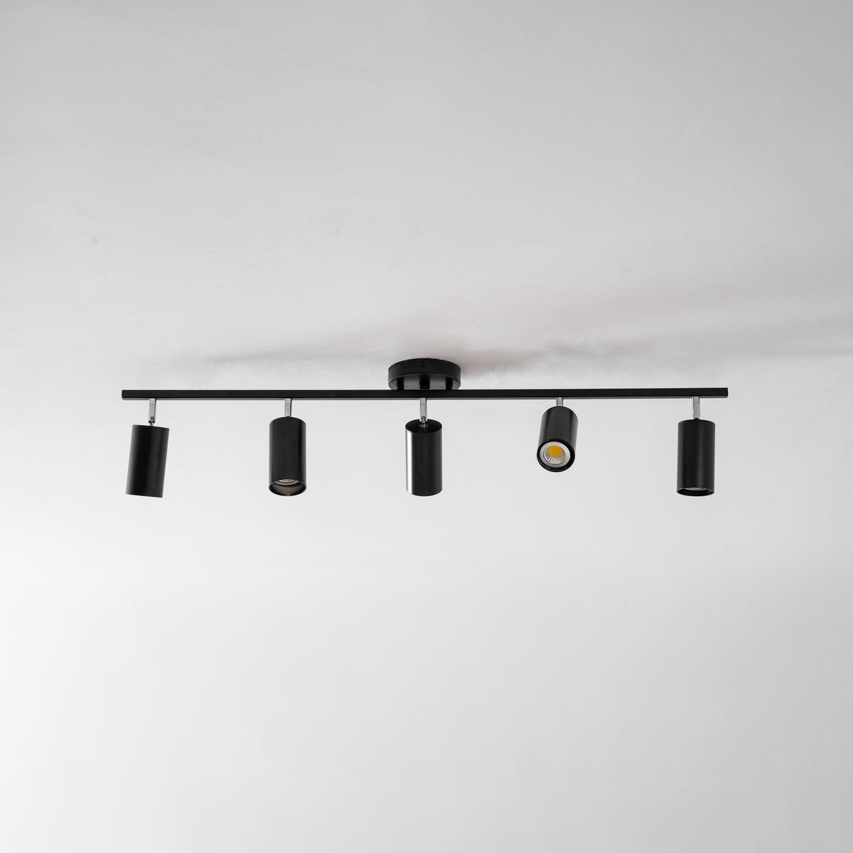 Overhead view of a black Clérachic five-head track light on a white ceiling, one head lit and the others pointing down.