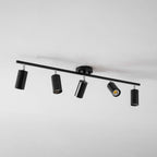 A black Clérachic five-head track light seen from an angle on a white ceiling, with one head glowing.