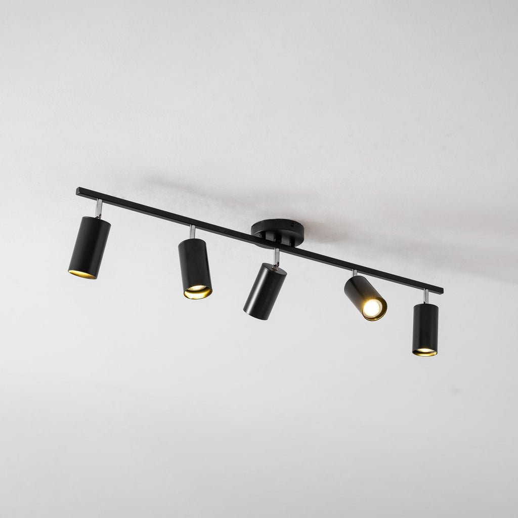 A black Clérachic five-head track light from below on a pale ceiling, its heads tilted in different directions.