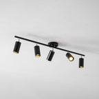 A black Clérachic five-head track light from below on a pale ceiling, its heads tilted in different directions.