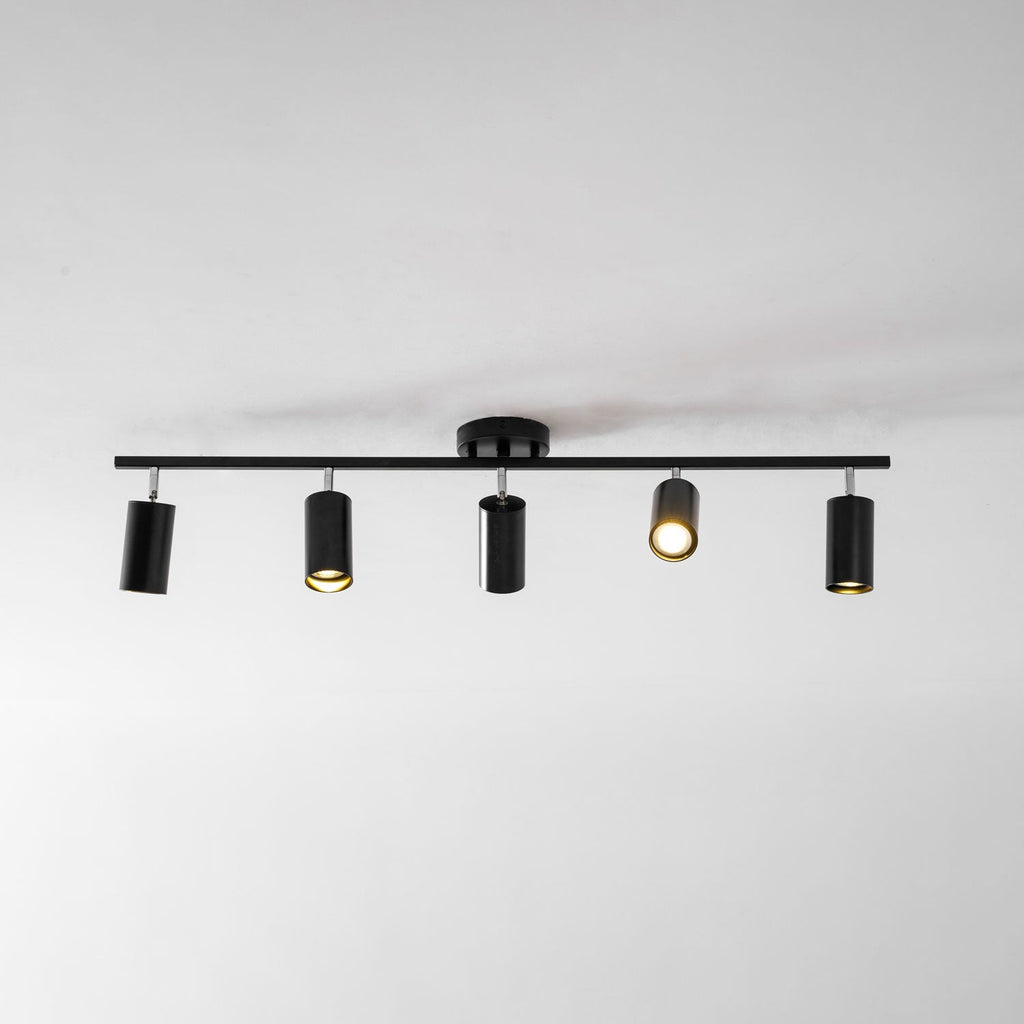 A black Clérachic track light with five heads on a white ceiling, one of them lit with a warm glow.