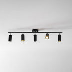 A black Clérachic track light with five heads on a white ceiling, one of them lit with a warm glow.