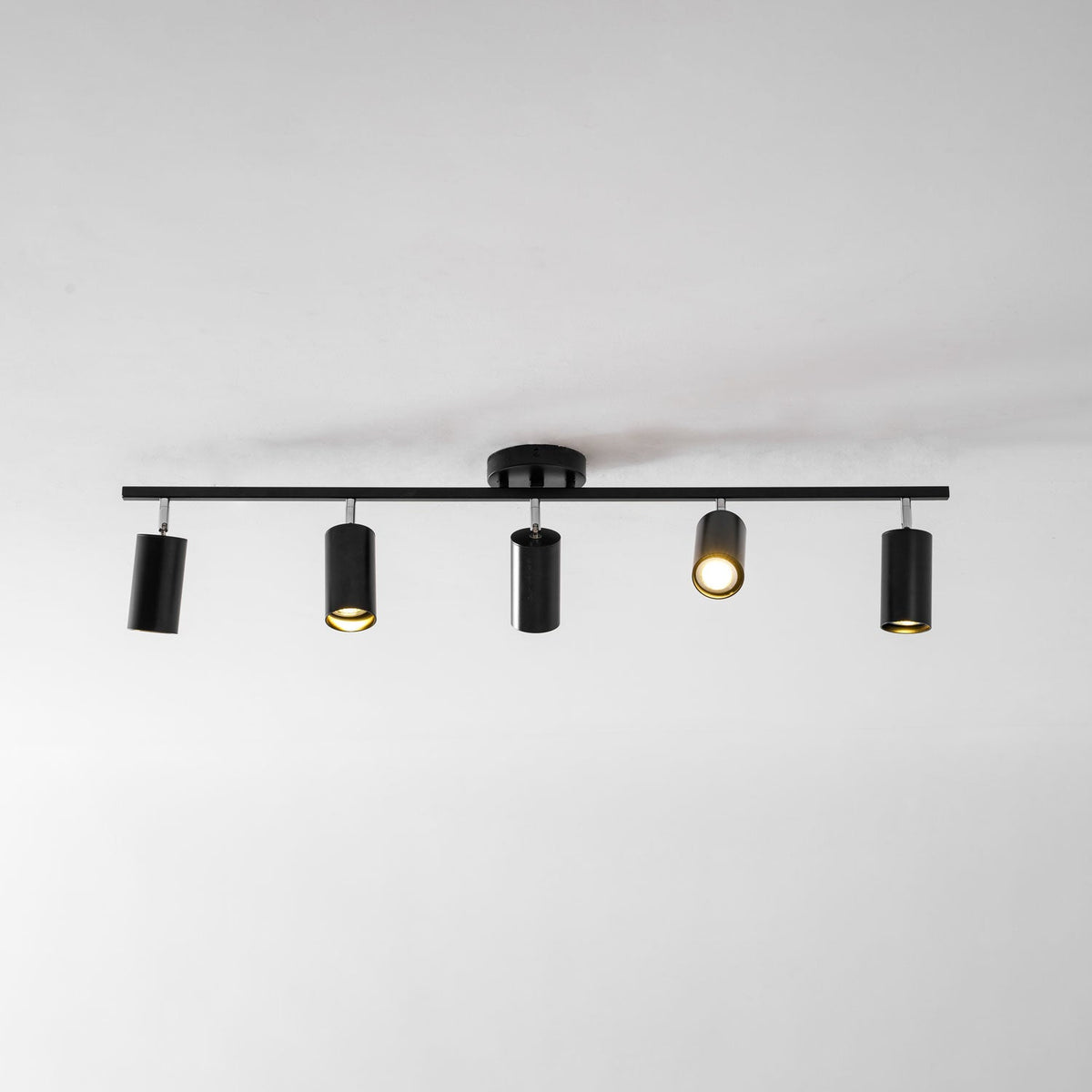 A black Clérachic track light with five heads on a white ceiling, one of them lit with a warm glow.