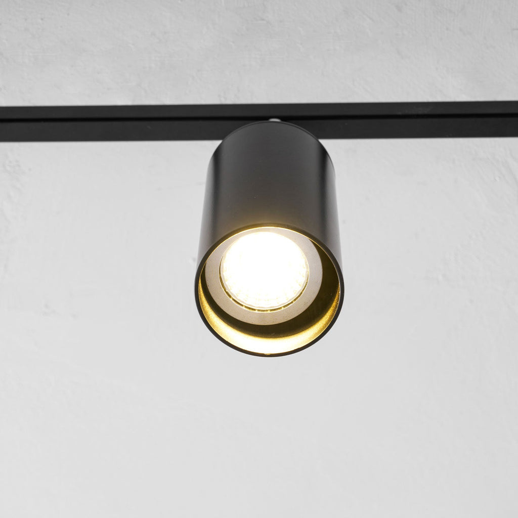 Close view of a black Clérachic spotlight head with a bright bulb inside a gold-lined cylinder.