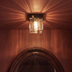 Close view of the Clérachic bubbled glass ceiling light lit warm, throwing streaked light over a wine-red wall and mirror frame.