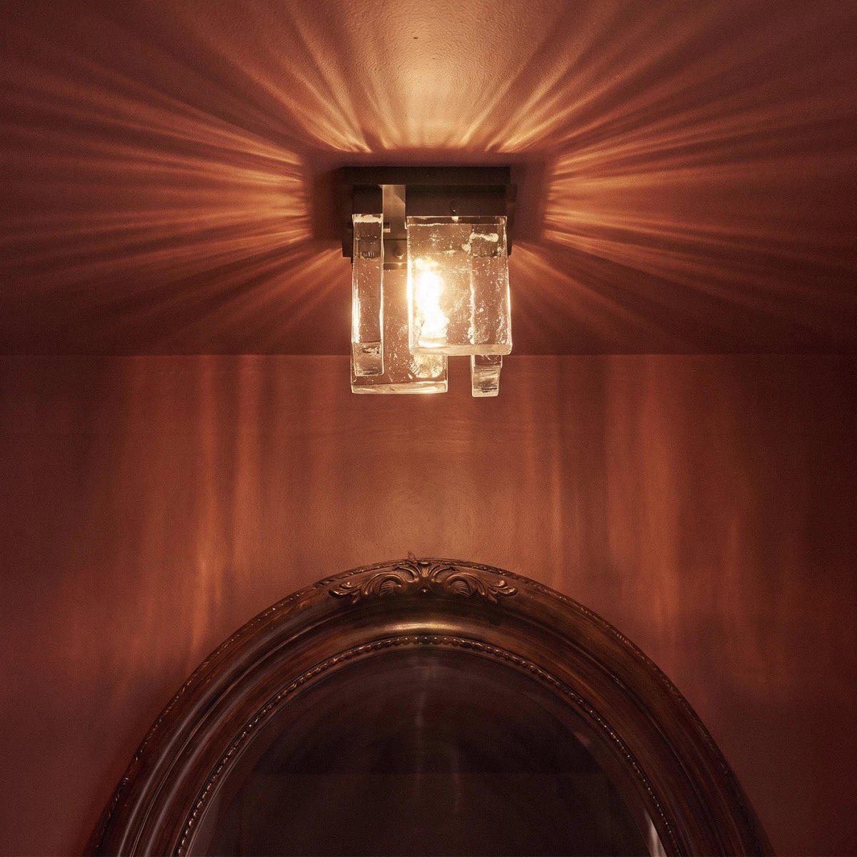 Close view of the Clérachic bubbled glass ceiling light lit warm, throwing streaked light over a wine-red wall and mirror frame.
