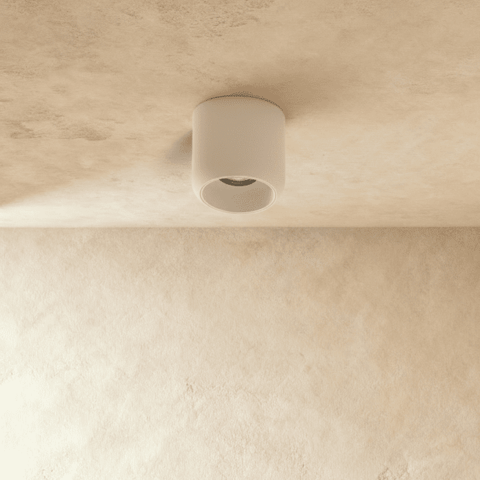 Clérachic downlight in white, the round cylinder housing catching light against a textured plaster ceiling.
