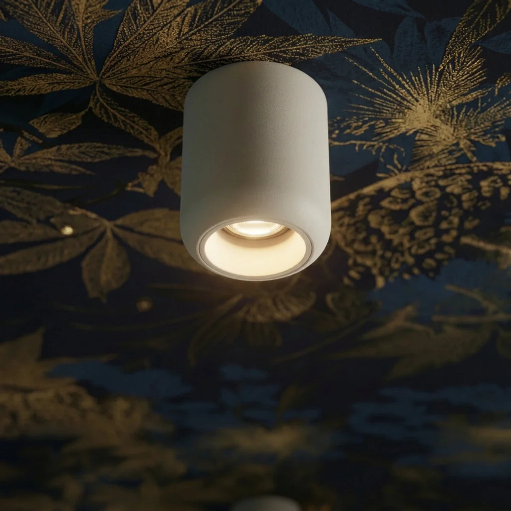 Close-up of a Clérachic downlight in white, its round beam glowing against a dark gold floral ceiling print.