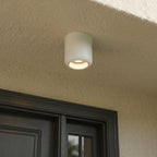 Close-up of a Clérachic downlight in white mounted under a covered entrance overhang above a dark front door.