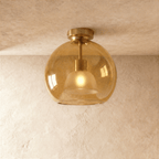 Clérachic amber hand-blown glass globe ceiling light flush-mounts to a plaster ceiling with a gold fitter.