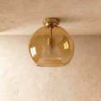 Clérachic wide amber glass globe ceiling light glows warm, its inner dome shade visible through the glass.