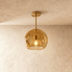 Clérachic amber glass globe pendant drops on a gold rod from the ceiling, inner dome shade lit warm inside.