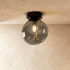 Clérachic smoked hand-blown glass globe with a dimpled texture flush-mounts on a plaster ceiling in black.