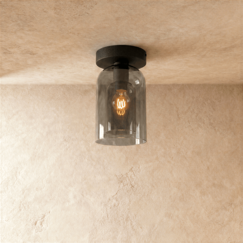 Clérachic smoked glass cylinder ceiling light flush-mounts in black, filament bulb glowing warm inside.