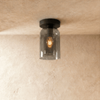 Clérachic smoked glass cylinder ceiling light flush-mounts in black, filament bulb glowing warm inside.