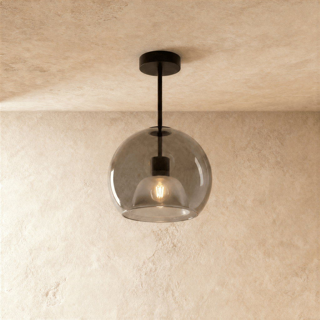 Clérachic smoked glass globe pendant drops on a black rod, its inner dome shade lit warm against the glass.