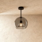 Clérachic smoked glass globe pendant drops on a black rod, its inner dome shade lit warm against the glass.