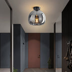 Clérachic smoked glass globe pendant hangs above a hallway with a terracotta door and slatted dark walls.