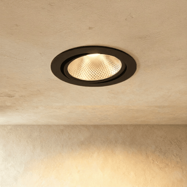 Clérachic downlight in black, its faceted reflector glowing warm white from a tiltable round ceiling trim.