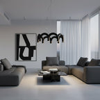 A black arched-tube Clérachic chandelier above a dark coffee table in a grey living room with a large black-and-white print.