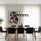 A black arched Clérachic chandelier above a wooden dining table with black chairs, in front of a large abstract canvas.