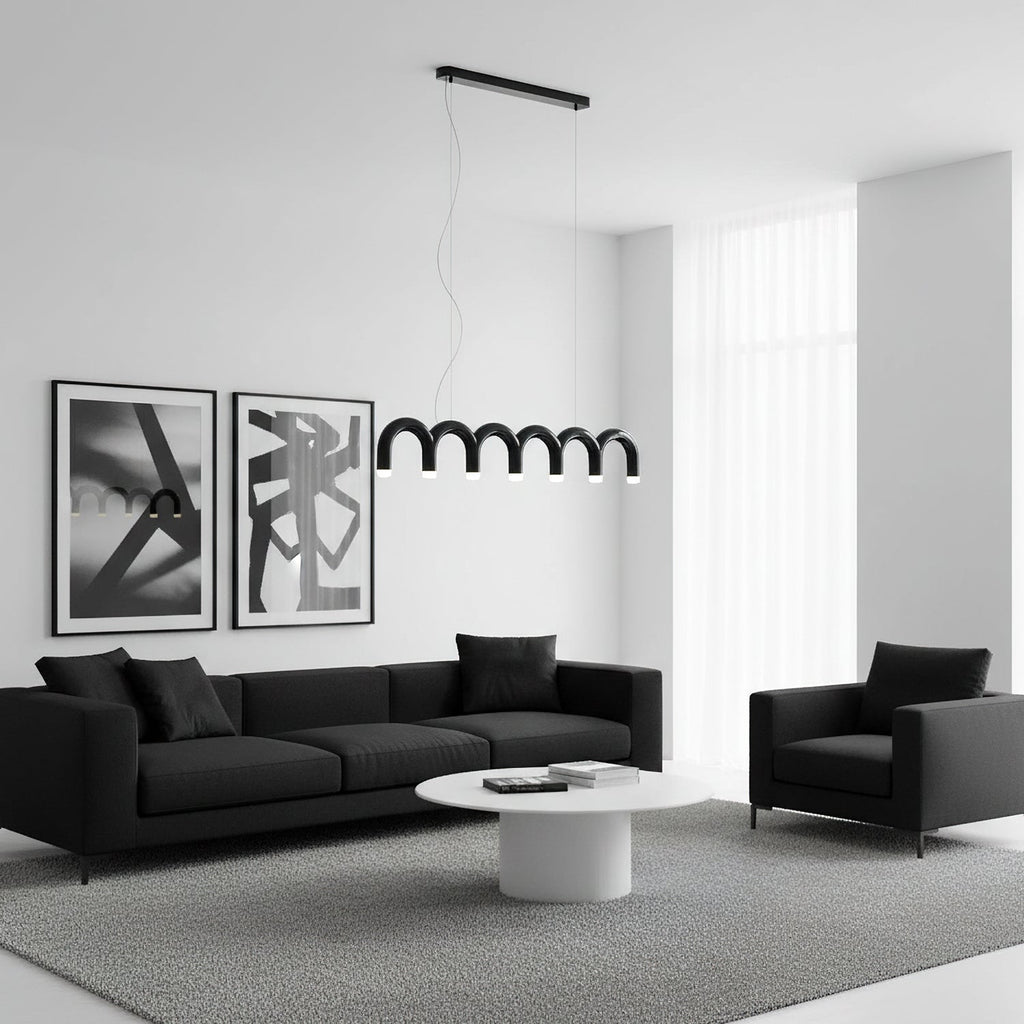 A black arched Clérachic chandelier hung low over a white round coffee table, with a black sofa and two framed prints behind.