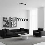 A black arched Clérachic chandelier hung low over a white round coffee table, with a black sofa and two framed prints behind.