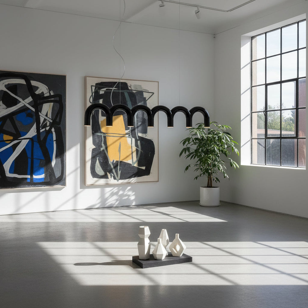 A black arched Clérachic chandelier in a bright gallery-style room, in front of two large abstract paintings.